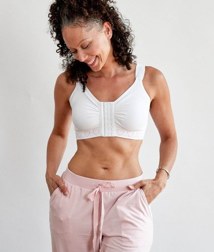 A woman wearing the cancer research  post surgery comfort bra with a front hook and eye fastening, in white