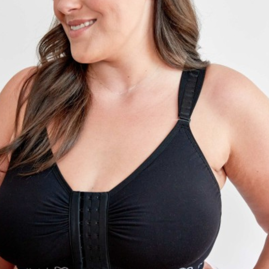 A woman wearing black post surgery mastectomy bra by cancer research uk, featuring a seamless design with wide, adjustable straps and a front hook and eye fastening and bi lateral pockets suitable for a softi immediately post surgery