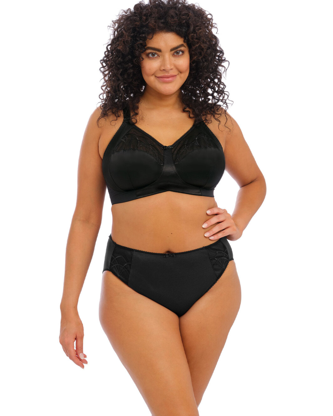 Elomi Cate Soft Cup Bra in black with sheer embroidery, soft satin cups, and an intersecting arc design. The bra offers three-piece cups with side support for shaping, uplift, and separation. It features a wide elastic underband, flexible side boning, and powernet wings for enhanced support. Complete with charming bow details, this bra combines elegance and comfort.