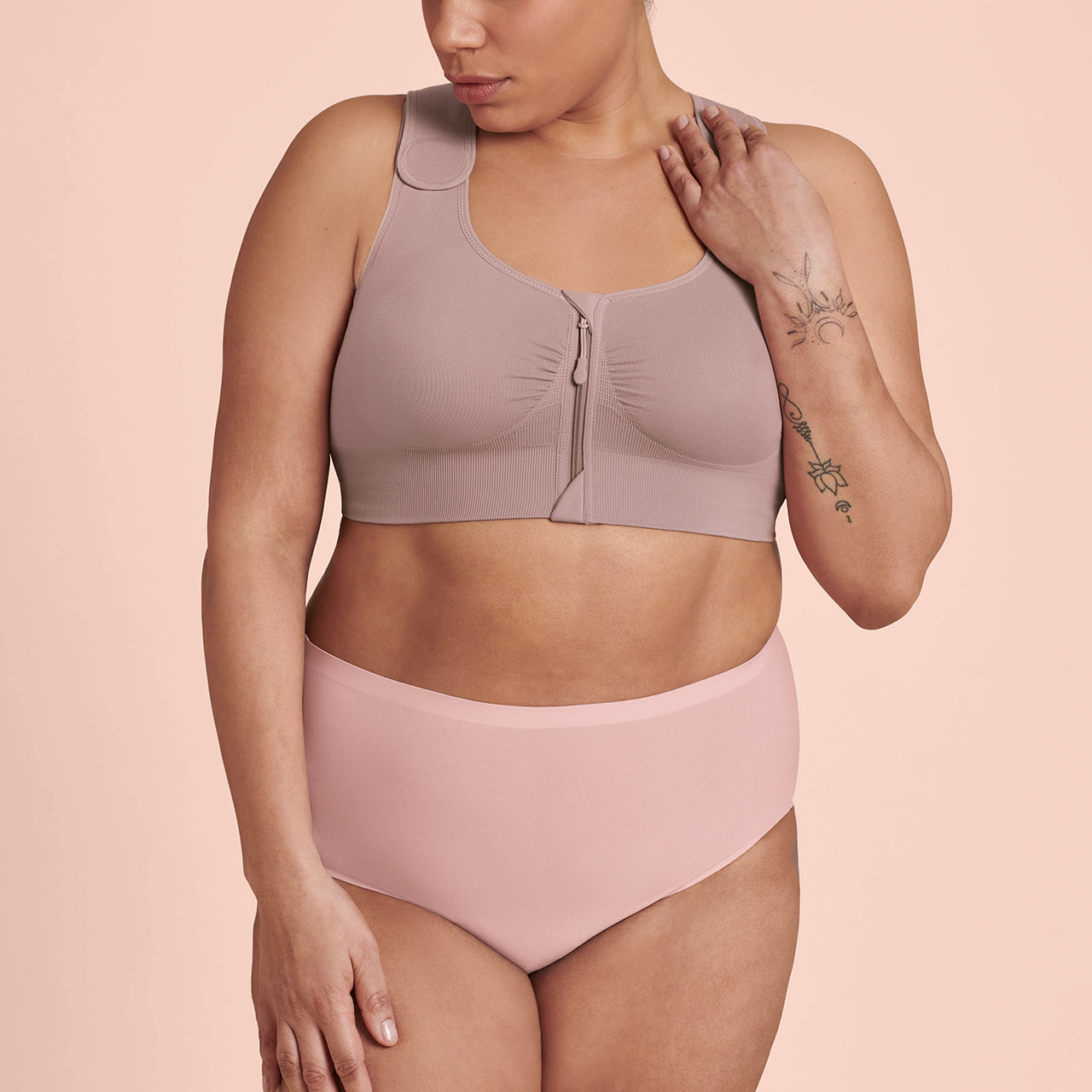 A woman wearing a mauve Anita Almeria Compression Bra, designed for post-surgery support, with a front zip closure and wide, adjustable straps.