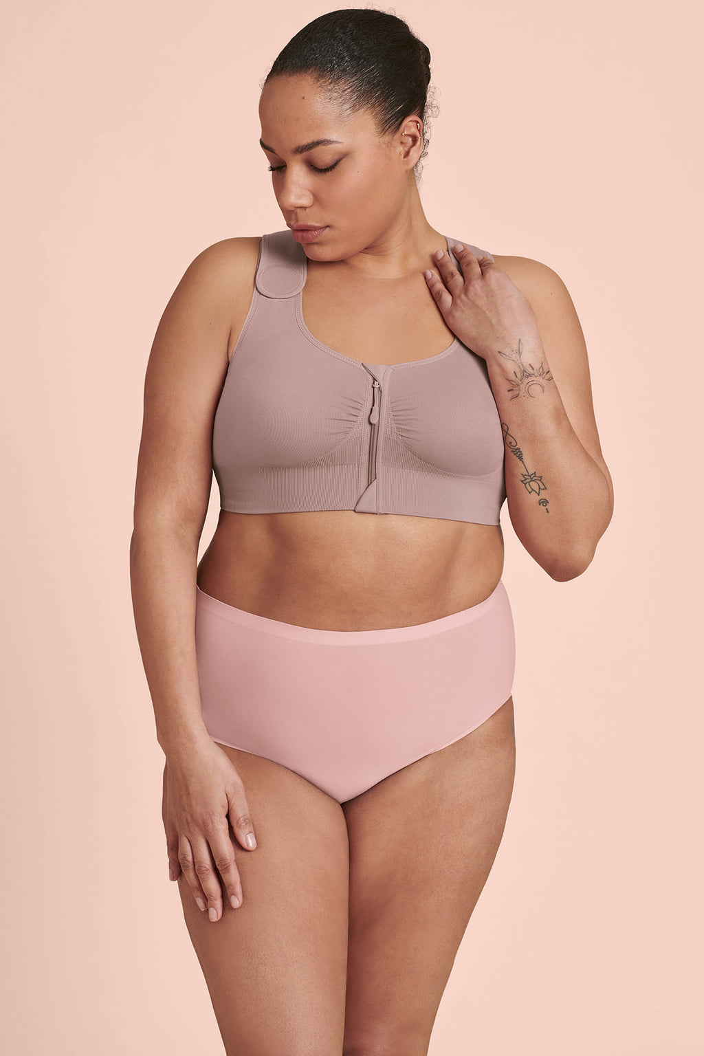 A woman wearing a mauve Anita Almeria Compression Bra, designed for post-surgery support, with a front zip closure and wide, adjustable straps.