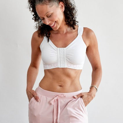 A woman wearing the cancer research  post surgery comfort bra with a front hook and eye fastening, in white 