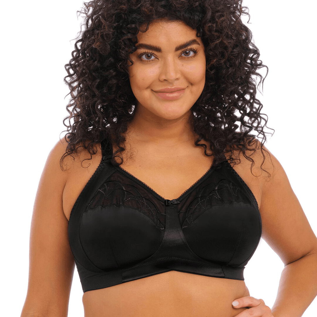 Elomi Cate Soft Cup Bra in black with sheer embroidery, soft satin cups, and an intersecting arc design. The bra offers three-piece cups with side support for shaping, uplift, and separation. It features a wide elastic underband, flexible side boning, and powernet wings for enhanced support. Complete with charming bow details, this bra combines elegance and comfort.
