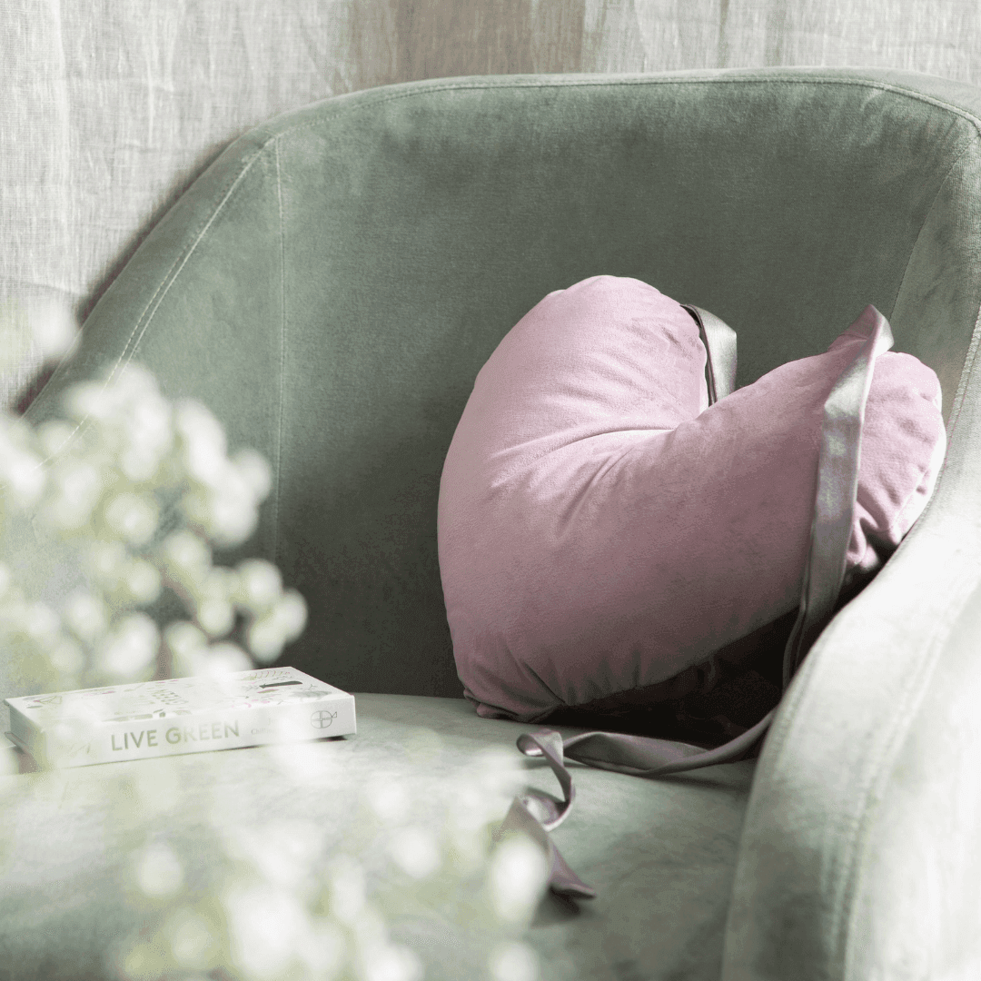 image showing the cancer research uk post surgery heart pillow in pink with grey satin ribbon on a green chair 