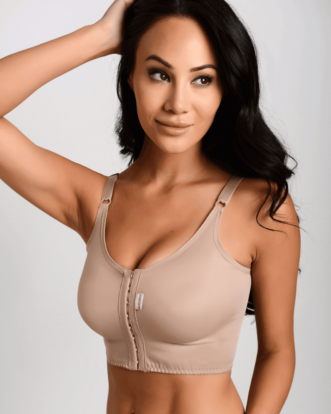 Woman wearing the Macom Signature bra in Clay. The Signature bra is suitable to be worn after most breast surgeries including augmentation and reduction. It features a hook and eye front fastening and thin adjustable straps for wardrobe versatility.